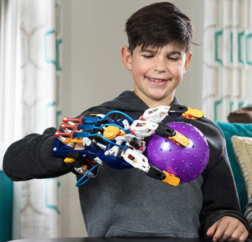 Boy using Mega Cyborg Hand model to grip a purple ball with mechanical hydraulic fingers.