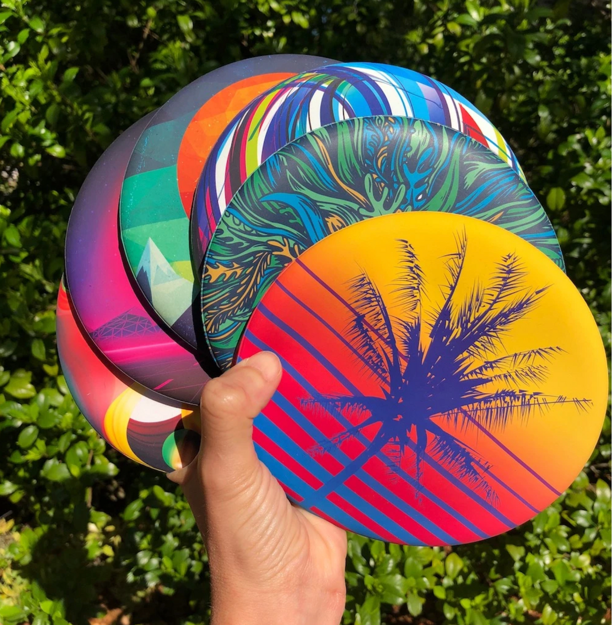 Hand holding multiple colorful Waboba Wingman Discs with nature background outdoors in sunlight
