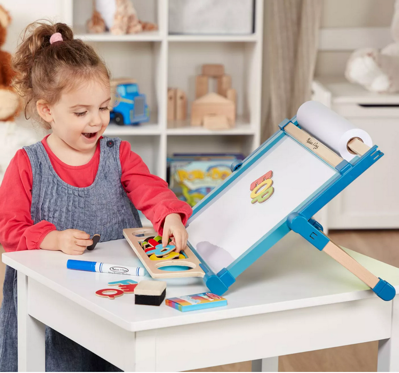 Child playing with a Magnetic Tabletop Easel featuring a dry-erase board, paper roll holder, and letter magnets.