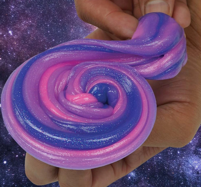 Hand stretching colorful shimmering Trendsetters Intergalactic Thinking Putty in deep space blue, ultraviolet purple, and cosmic pink.