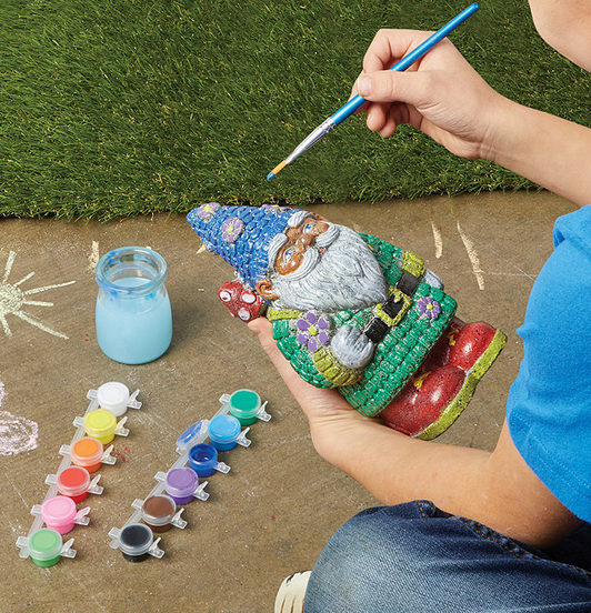 Person painting a colorful, hand-painted PYO Stone Gnome with vibrant paints outdoors on a patio.