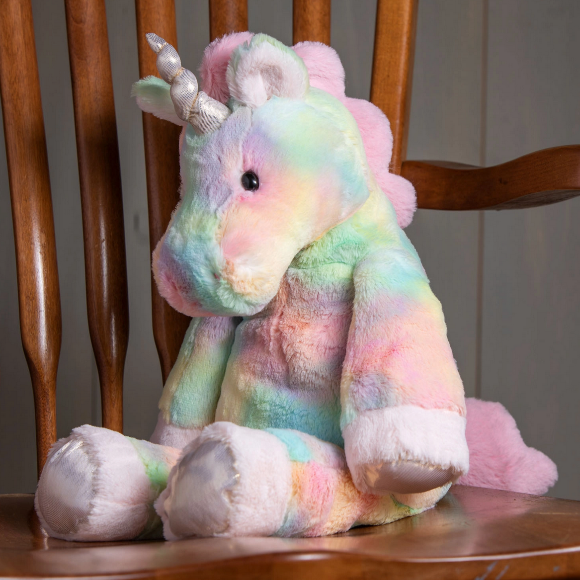 Plush pastel rainbow Marshmallow Fro-Yo Unicorn sitting on wooden chair with soft fabric and embroidered details.