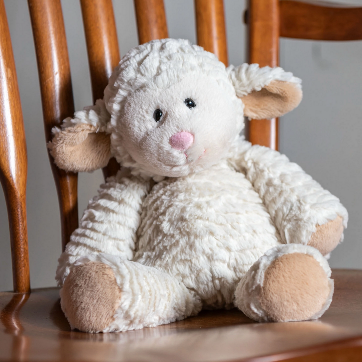 Marshmallow Lamb soft plush toy with embroidered face and weighted filling sitting on a wooden chair for comfort.