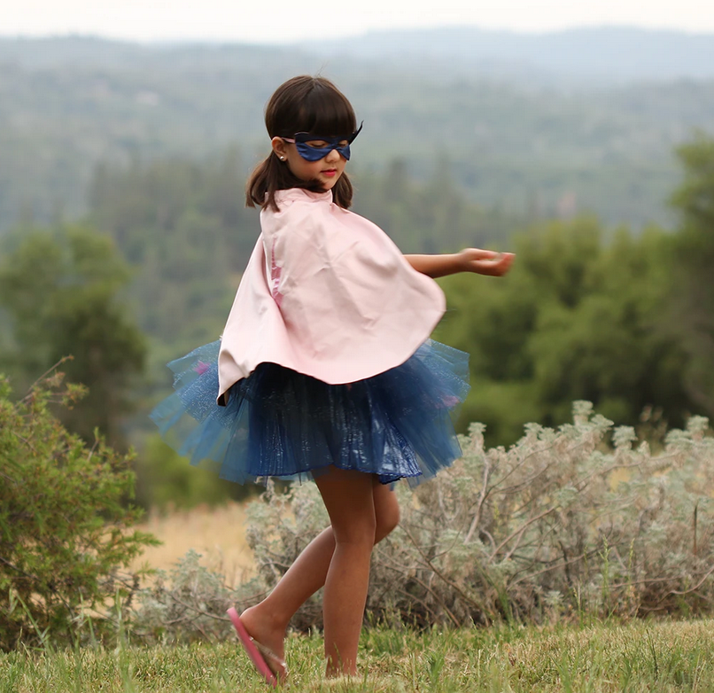 Girl twirling outdoors wearing the Super Duper Tutu, Cape & Mask with navy tutu and pink cape.