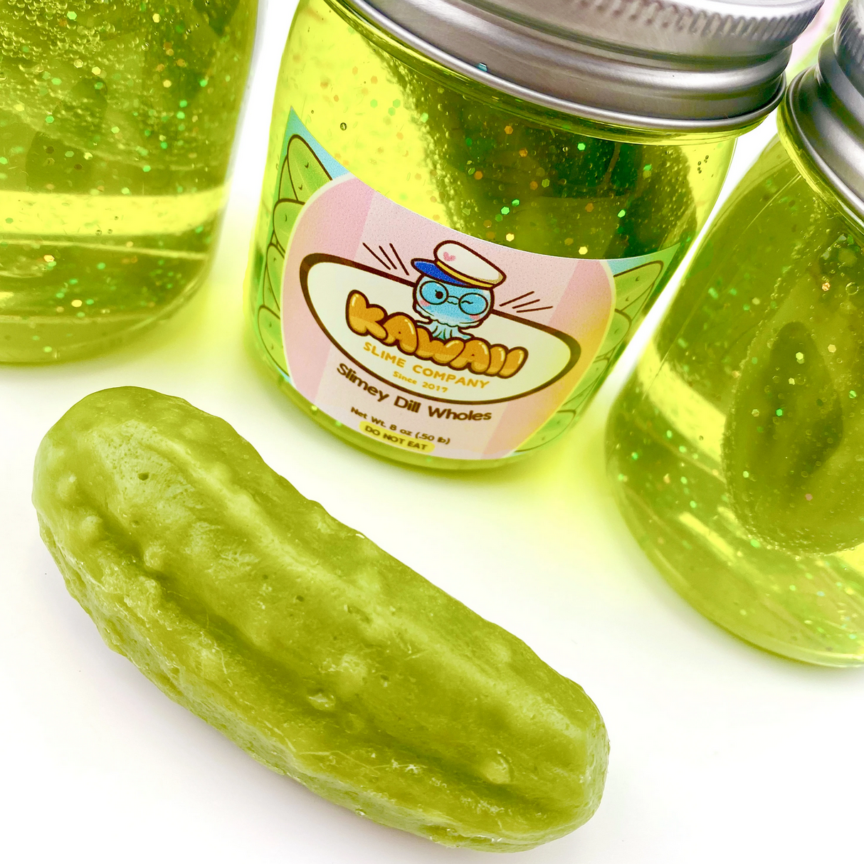 Shimmery Pickle Clear Slime in jars with glittery stretchy slime and a realistic pickle eraser beside them.
