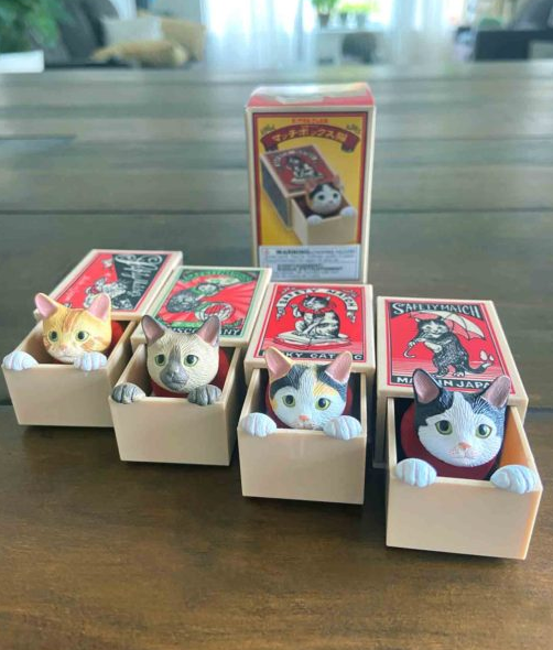 Cat Peek Matchbox Blind Box showing four detailed cat figurines peeking out from their matchboxes on a wooden table.