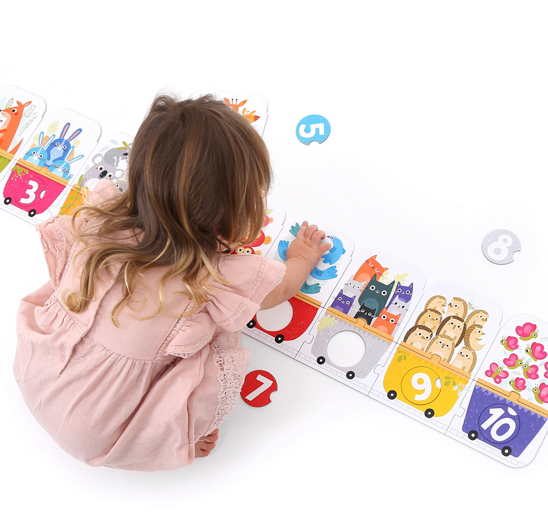 Child assembling the 30pc Matching Number Train Floor Puzzle with colorful animal wagons and number circles.