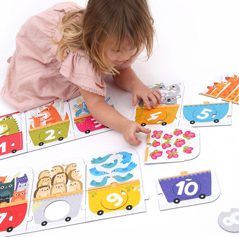 Young child assembling colorful 30pc Matching Number Train Floor Puzzle with animal-themed wagons and numbers.