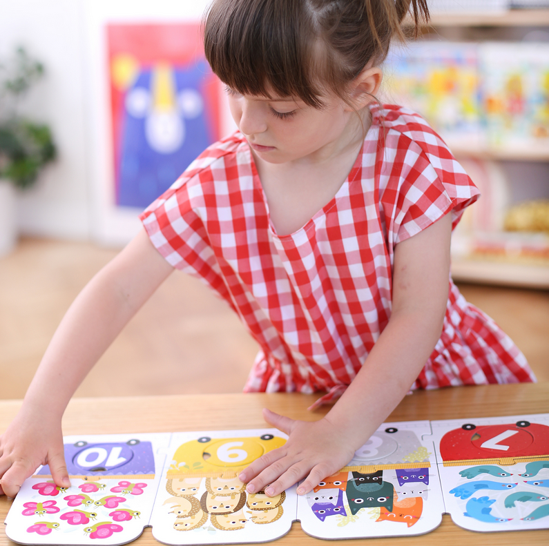 Child playing with 30pc Matching Number Train Floor Puzzle featuring colorful animal and number pieces on a wooden table.