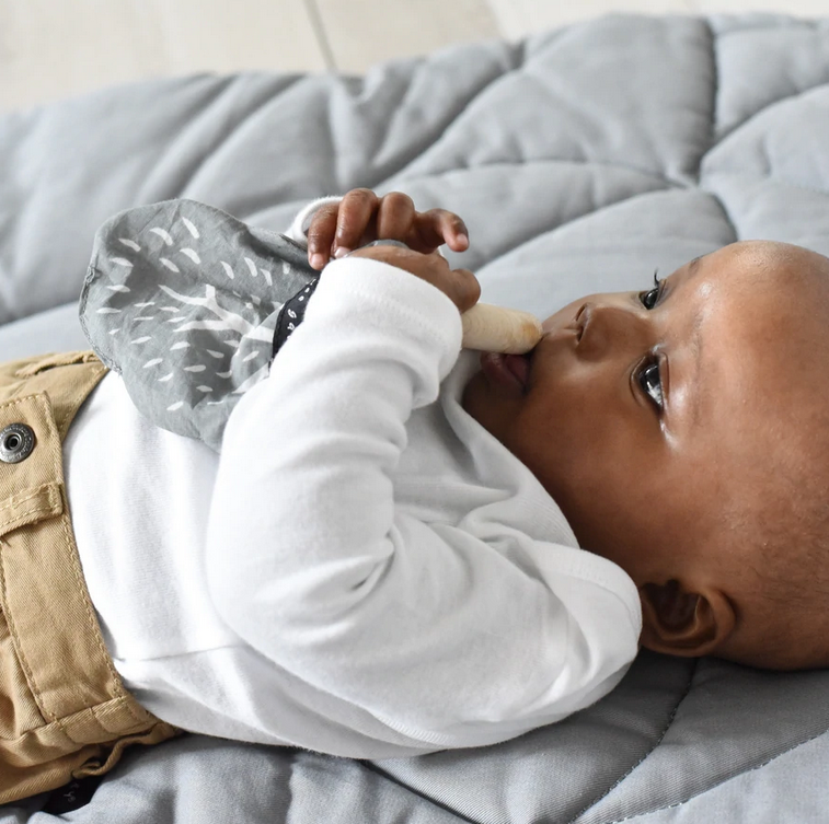Baby lying down holding and chewing on the Organic Crinkle Teether | Acorn with maple wooden ring and cotton fabric.