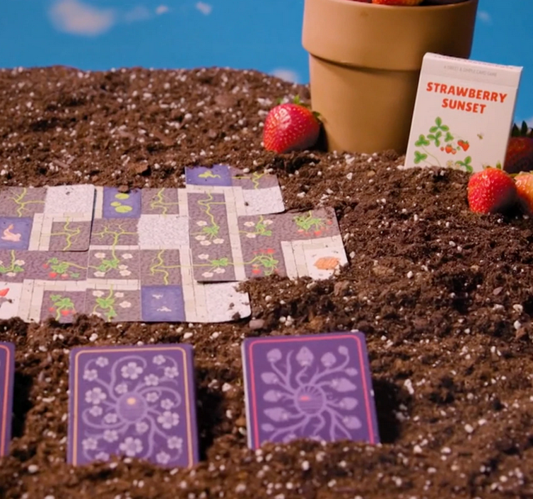 Strawberry Sunset game setup with soil, strawberry plants, cards, and a flower pot in a friendly garden scene.
