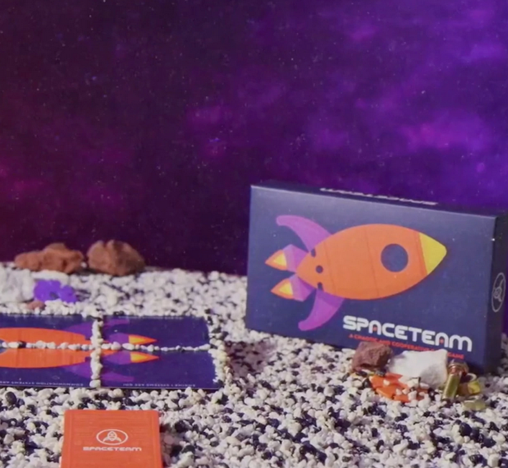 Spaceteam card game box and cards displayed on rocky surface with a purple starry space background.