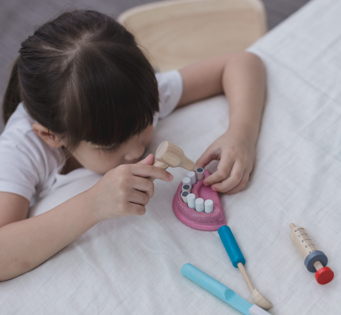 Child playing with wooden teeth and tools from the Dentist Set for pretend dental care and hygiene learning.