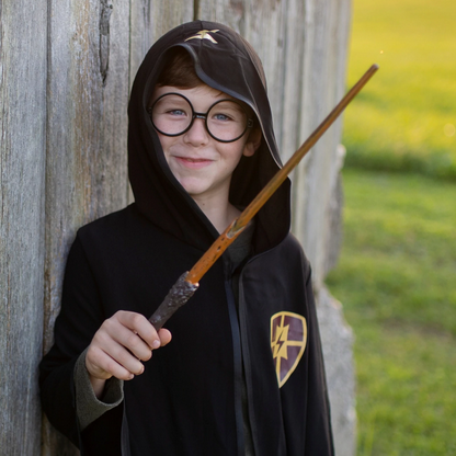 Child dressed as a wizard holding a Wizard Wand with a dark brown handle and wooden-inspired tip outdoors.