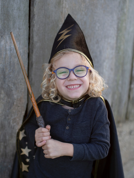 Child smiling while holding a Wizard Wand with dark brown handle and wooden tip dressed as a young wizard