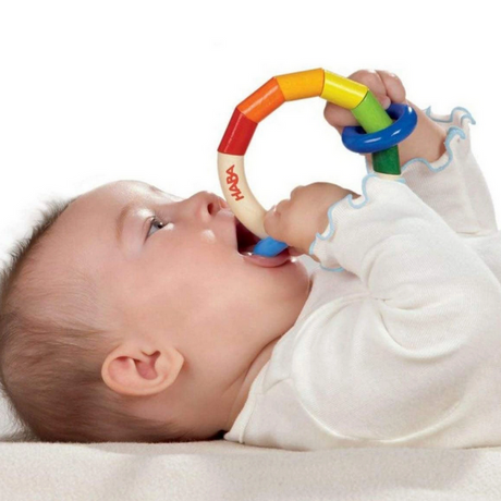 Baby lying down holding and mouthing the colorful hand-crafted Clutching Kringelring teething toy.