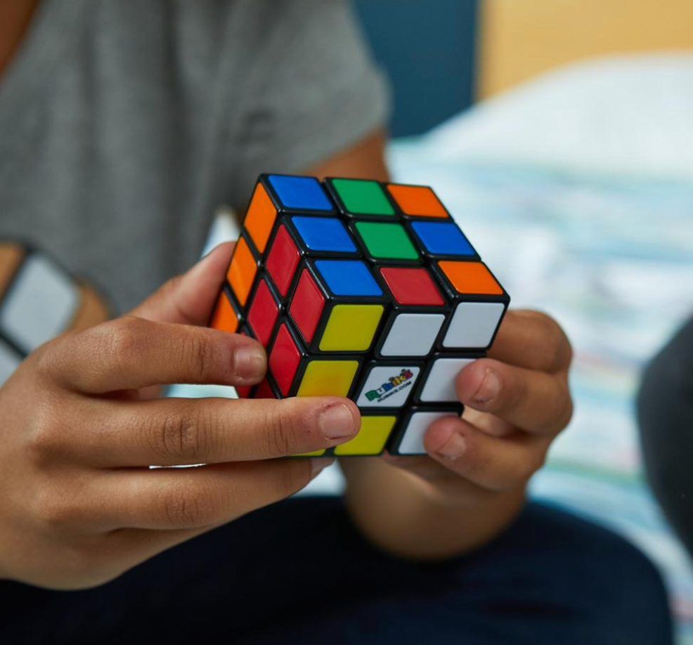 Close-up of hands solving a colorful Rubiks Cube puzzle, the world's most famous plastic cube toy.