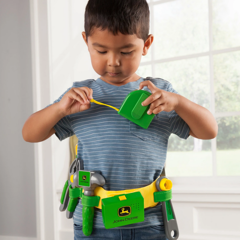 Young child wearing the John Deere Talking Tool Set with yellow belt and green toy tools playing indoors.