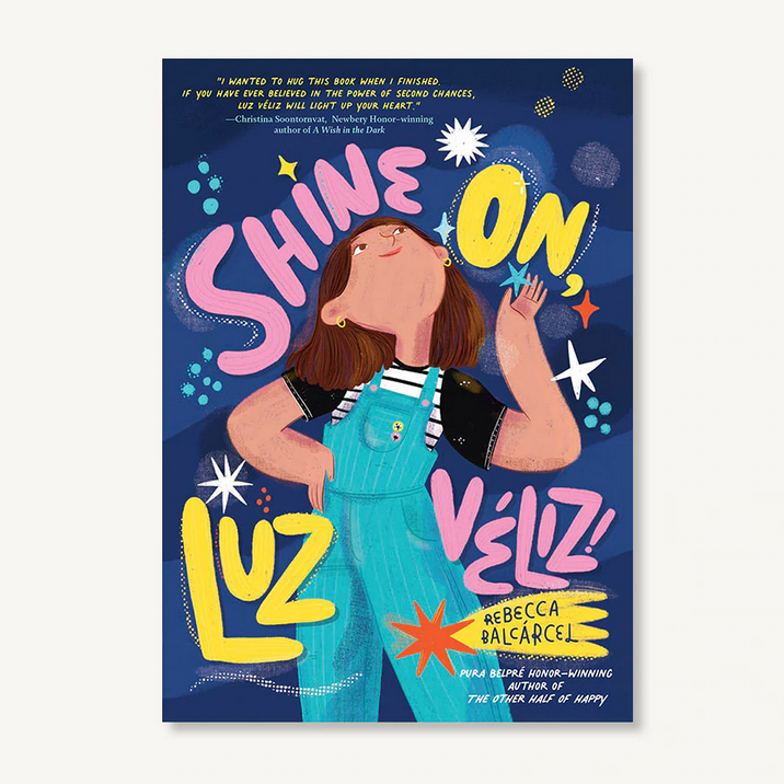 Book cover of Shine On, Luz Veliz! featuring a girl in overalls reaching toward a glowing star on a dark blue background.