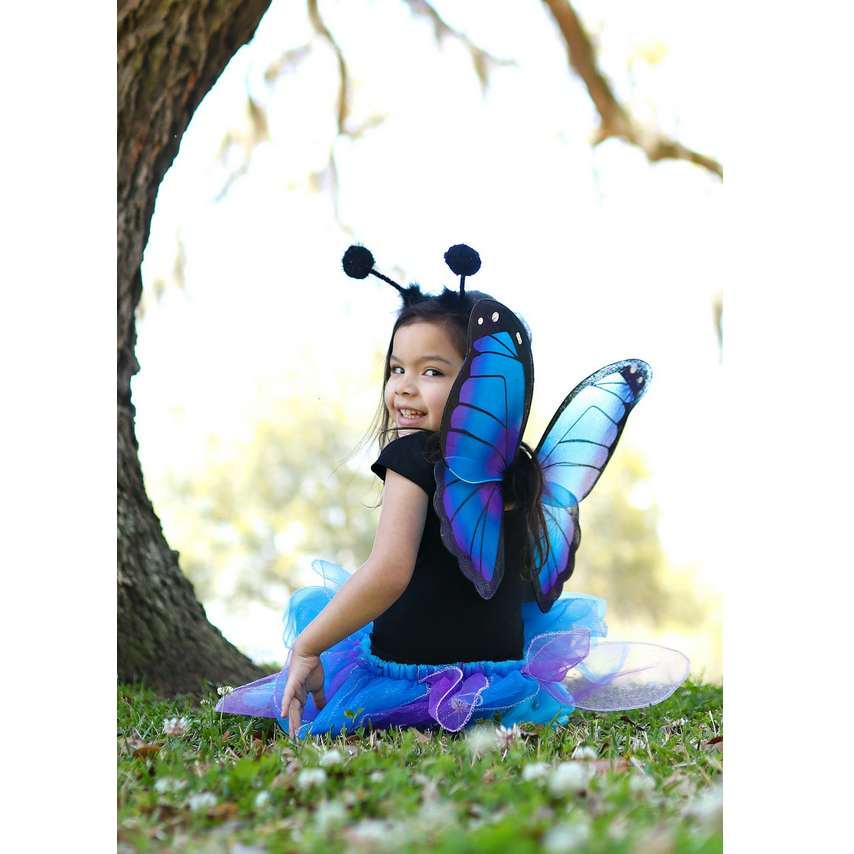Smiling child wearing the Midnight Butterfly Set with vibrant blue wings, glitter skirt, and butterfly antennae headband outdoors.