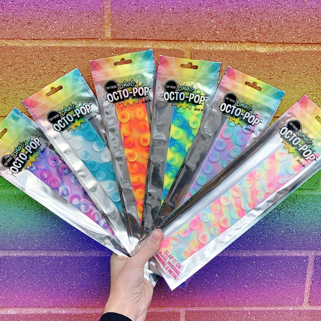 Hand holding assorted OMG Octopop Tie Dye suction cup fidget toys in colorful packaging against rainbow wall background