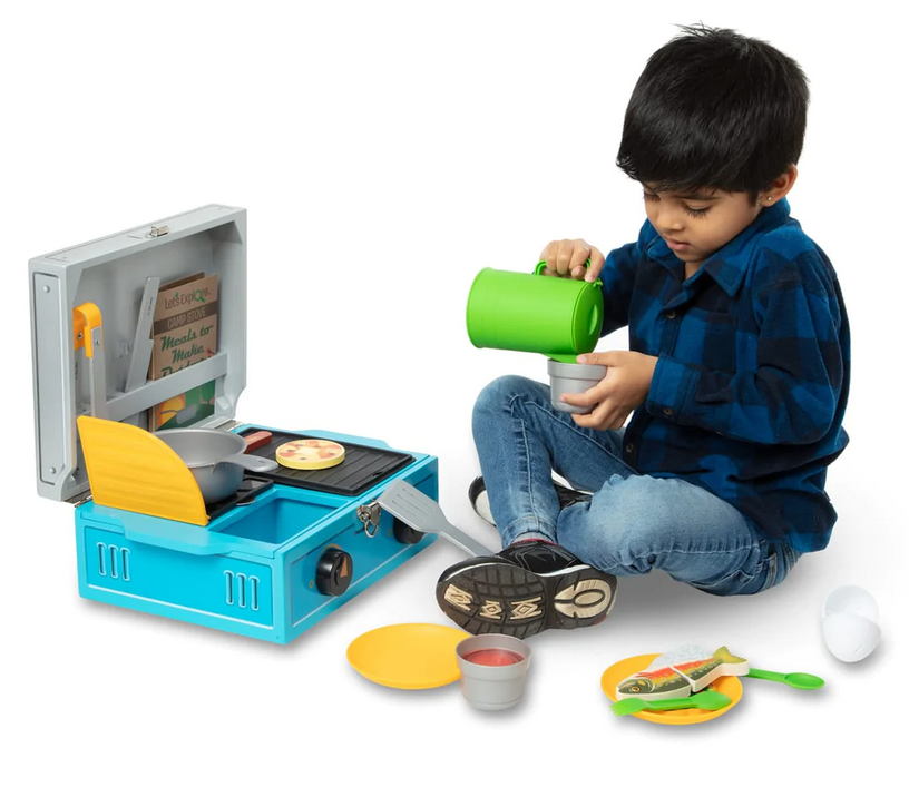 Child playing with Melissa & Doug Camp Stove Play Set, including stove, play food, utensils, and cups for imaginative outdoor cooking.