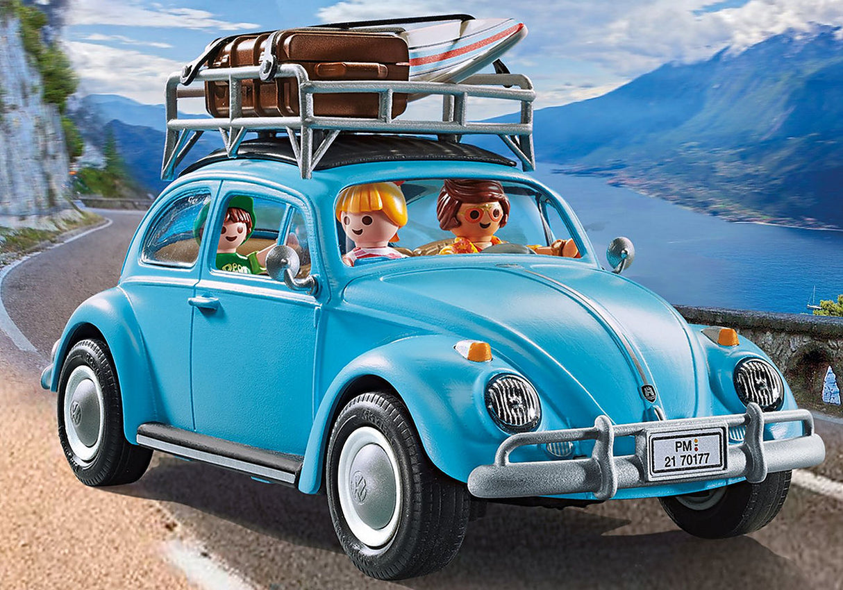 Volkswagen Beetle toy with roof rack, surfboard, and three figures on a scenic coastal road trip.