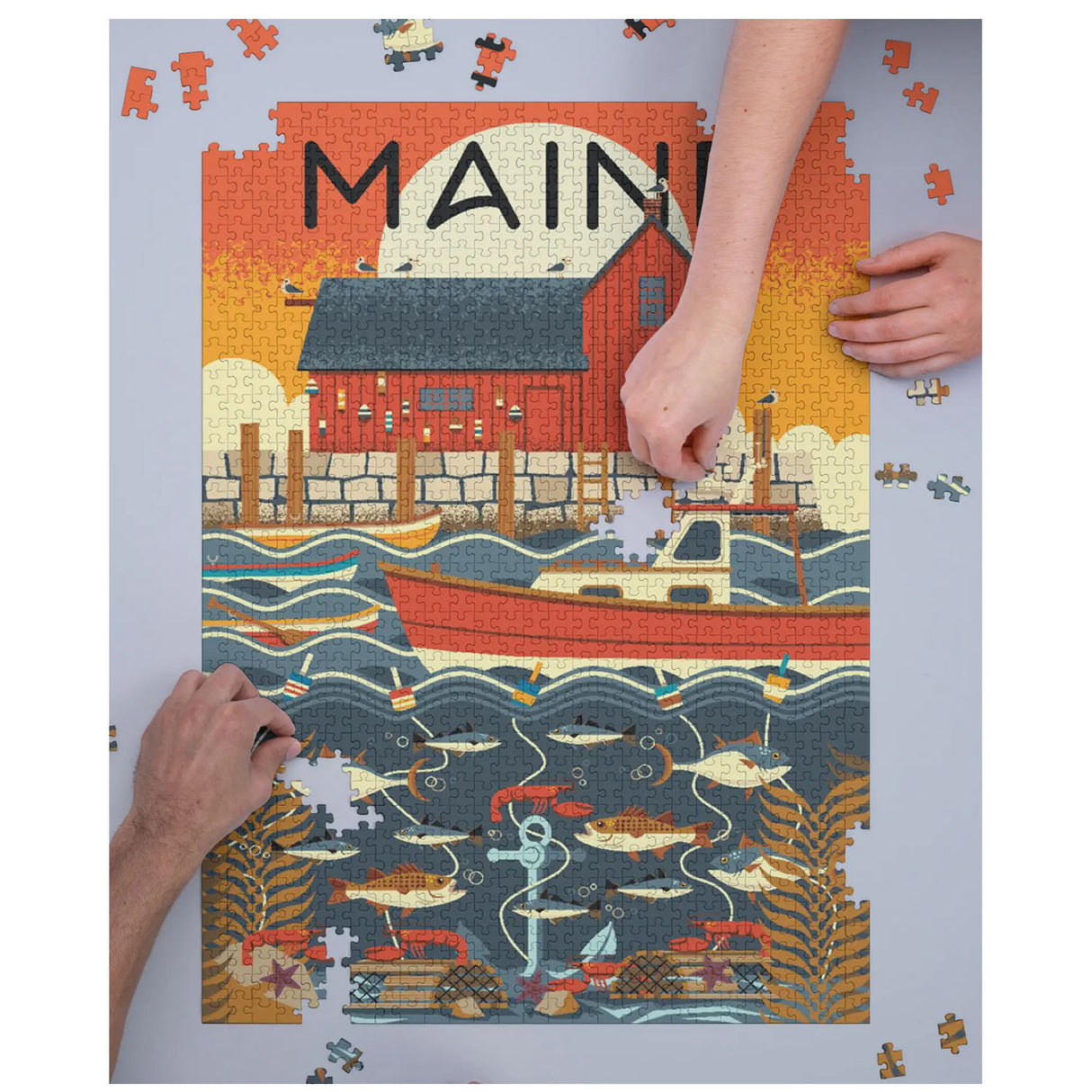 Hands assembling the colorful 1000pc Geometric Maine Puzzle featuring a Maine port scene.