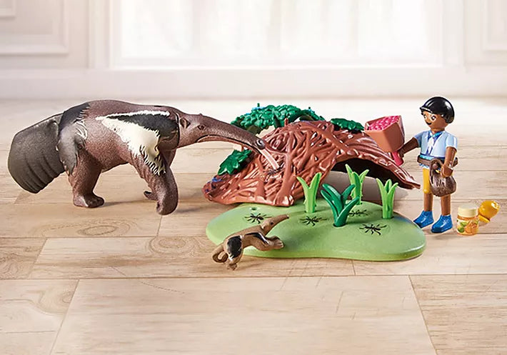 Two children figures care for anteater and baby near anthill with plants and accessories on wooden floor