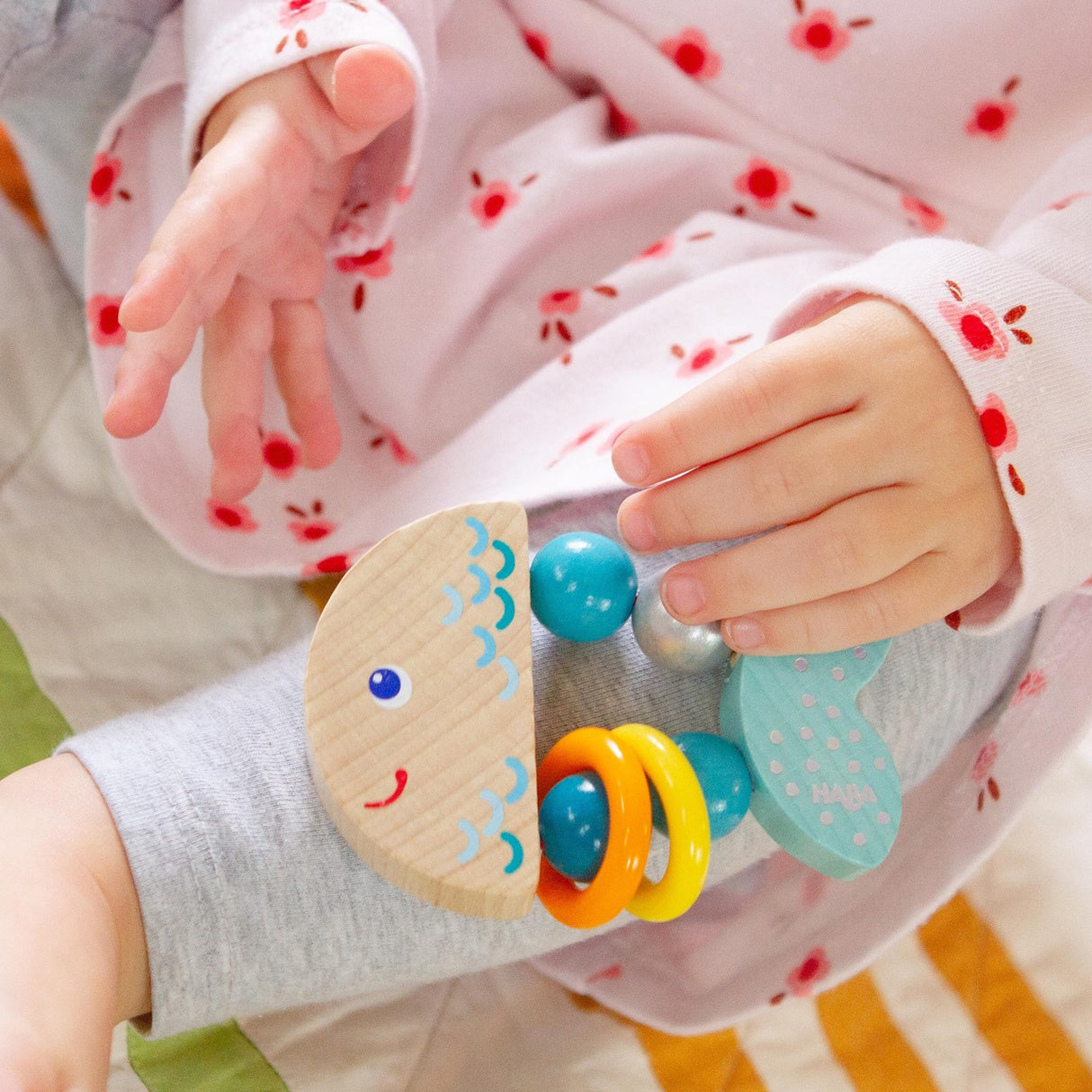 Baby holding Clutching Rattlefish wooden toy with colorful plastic rings, perfect for 6-18 months infants.