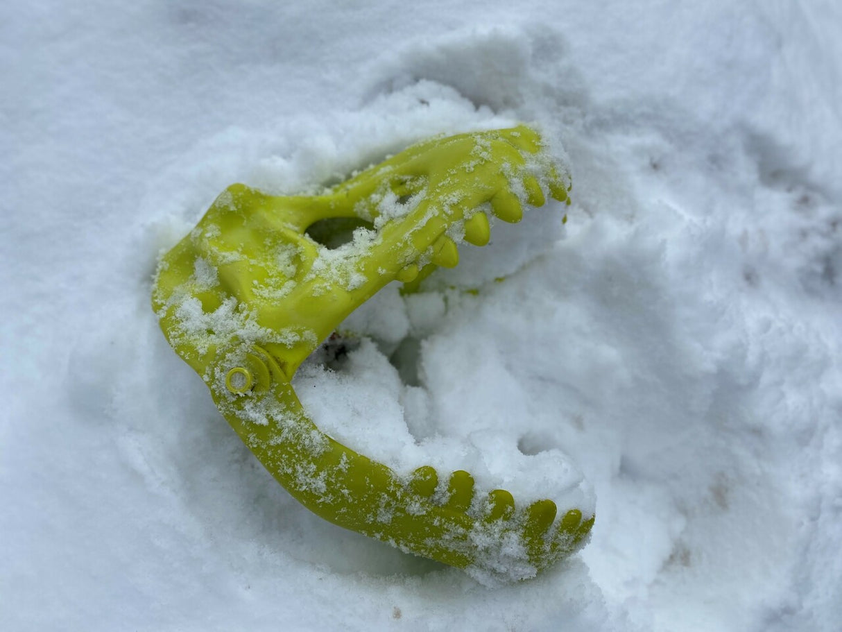 Green Dinosaur Sand Glove partially buried in snow, designed for kids to dig and play outdoors.