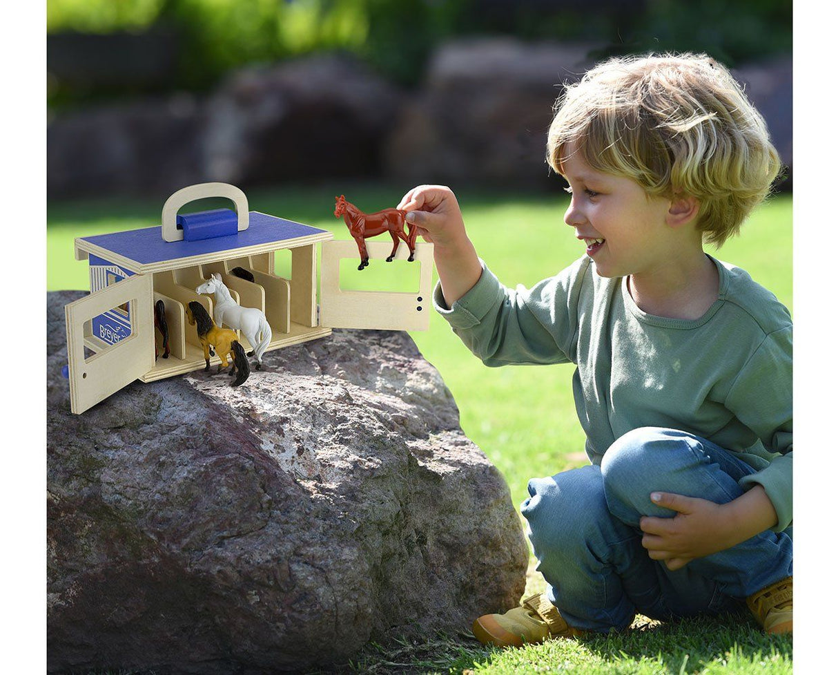 Child playing outdoors with the Stablemates Wooden Stable Set and small wooden horses near a rock.