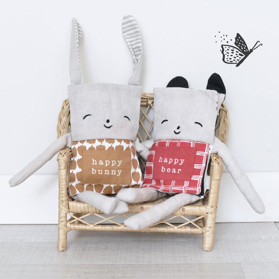 Organic Flippy Friend | Bear plush toy featuring a smiling face and red patterned outfit, sitting on a wicker chair.