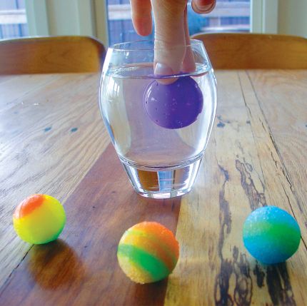 Bouncing Ball Kit with colorful high-bouncing balls, showing a purple ball being pressed into water on a wooden table.