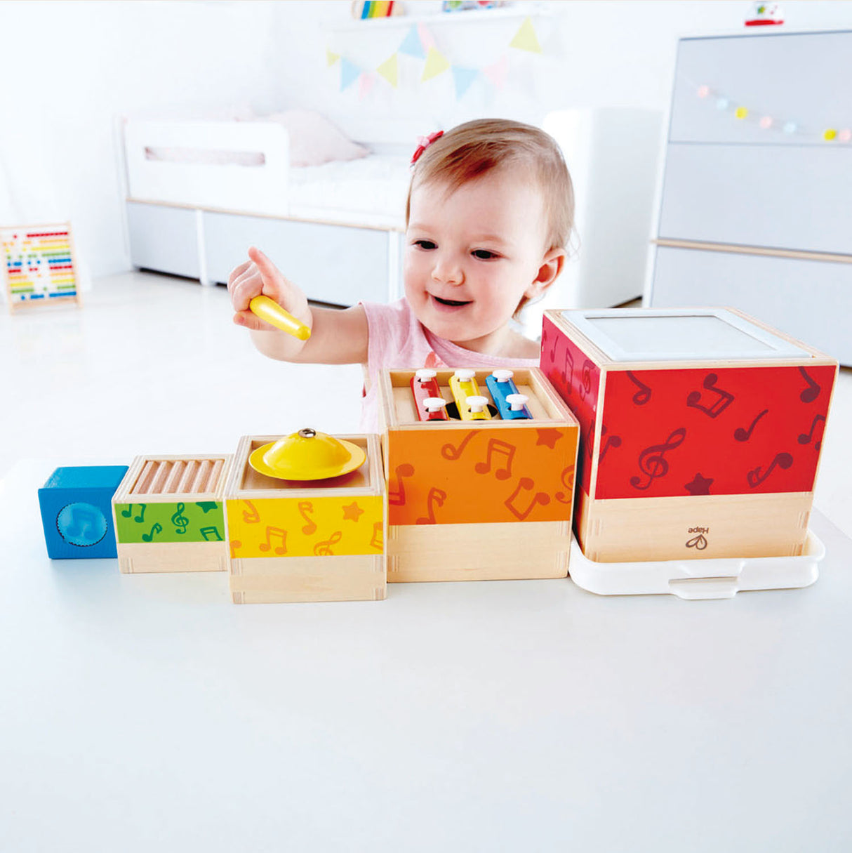 Smiling toddler playing with colorful stacking blocks and instruments in the Stacking Music Set for ages 18 months plus.