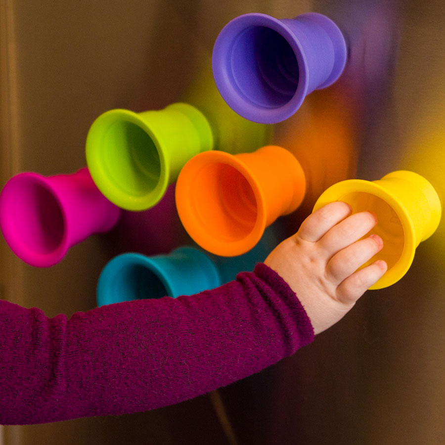Child’s hand attaching colorful suction silicone cups to a metal surface, showcasing Suction Kupz.