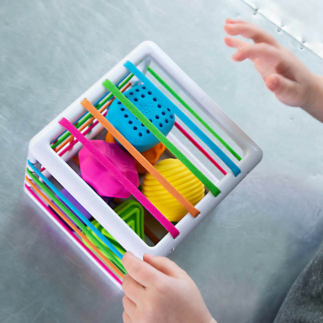 Inny Bin with six colorful, textured shapes and elastic bands sparks tactile learning and fine motor skills for toddlers.