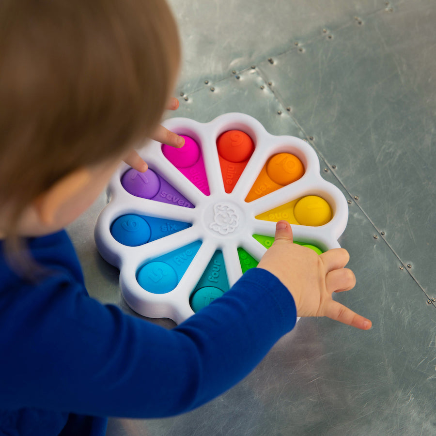 Child playing with colorful Dimpl Digits silicone number-learning toy with tactile bubbles for counting and motor skills.