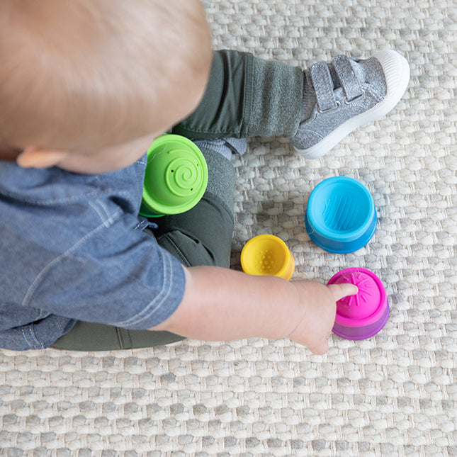 Child playing with colorful Dimpl Stack cups featuring textured silicone bubbles for tactile exploration and stacking fun