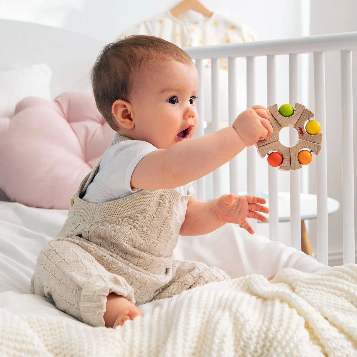 Baby sitting on bed playing with colorful Ball Wheel Grasping Toy with rattling balls for ages 6 months and up.
