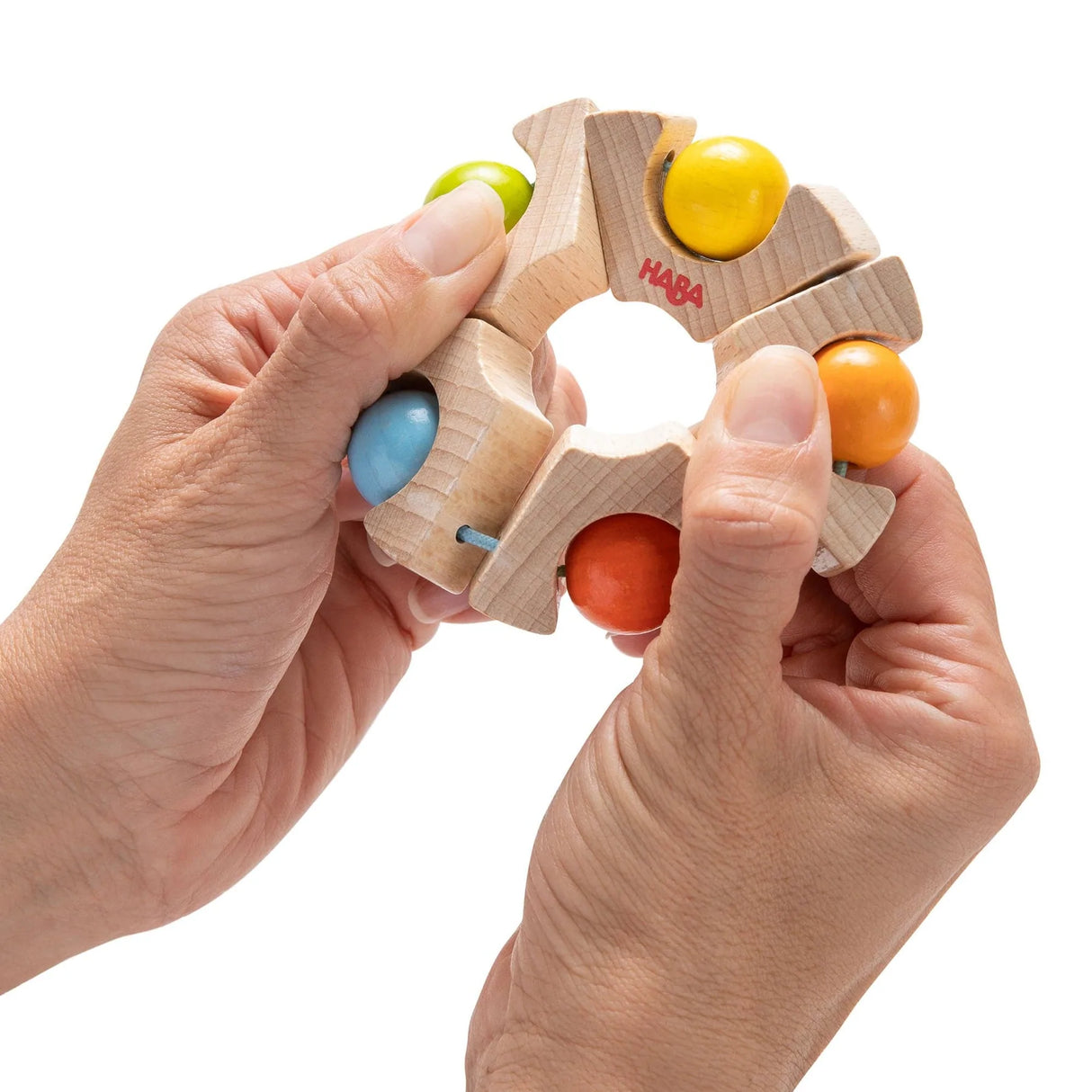 Hands holding a wooden Ball Wheel Grasping Toy with colorful rattling balls for babies ages 6 months and up.