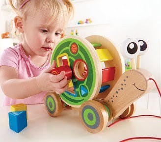 Child playing with colorful Pull Along Snail Sorter wooden toy featuring shape sorting blocks and pull string.