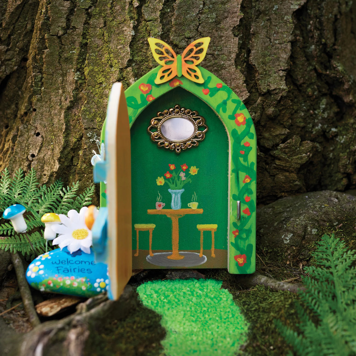 Butterfly Fairy Door with painted green arch, butterfly on top, tiny table scene inside, and fairy garden accessories outdoors.