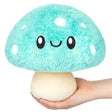 Soft turquoise mushroom plush with smiling face held in hand, Turquoise Mushroom Mini measuring 9 inches tall.
