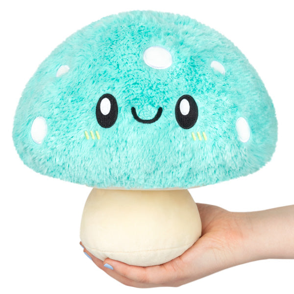 Soft turquoise mushroom plush with smiling face held in hand, Turquoise Mushroom Mini measuring 9 inches tall.