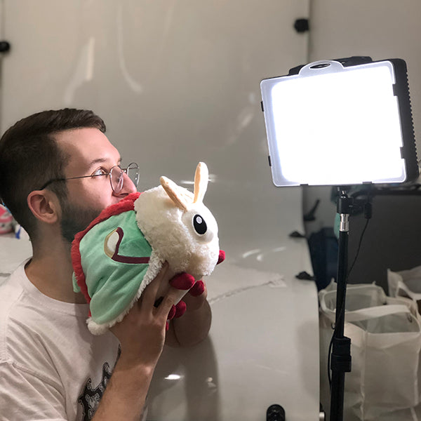 Man holding and looking at a colorful Luna Moth Mini plush toy near a bright studio light on a tripod