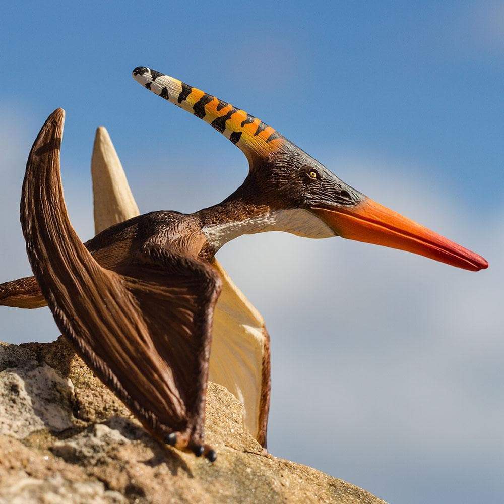 Pteranodon figure posed at rest on rock, showing large crest and detailed wings against blue sky background.