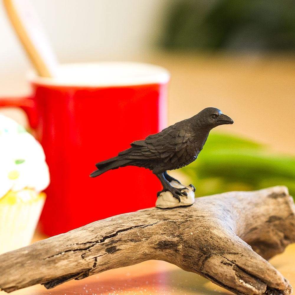Raven figurine perched on driftwood, detailed and hand-painted, perfect for décor or creative play.