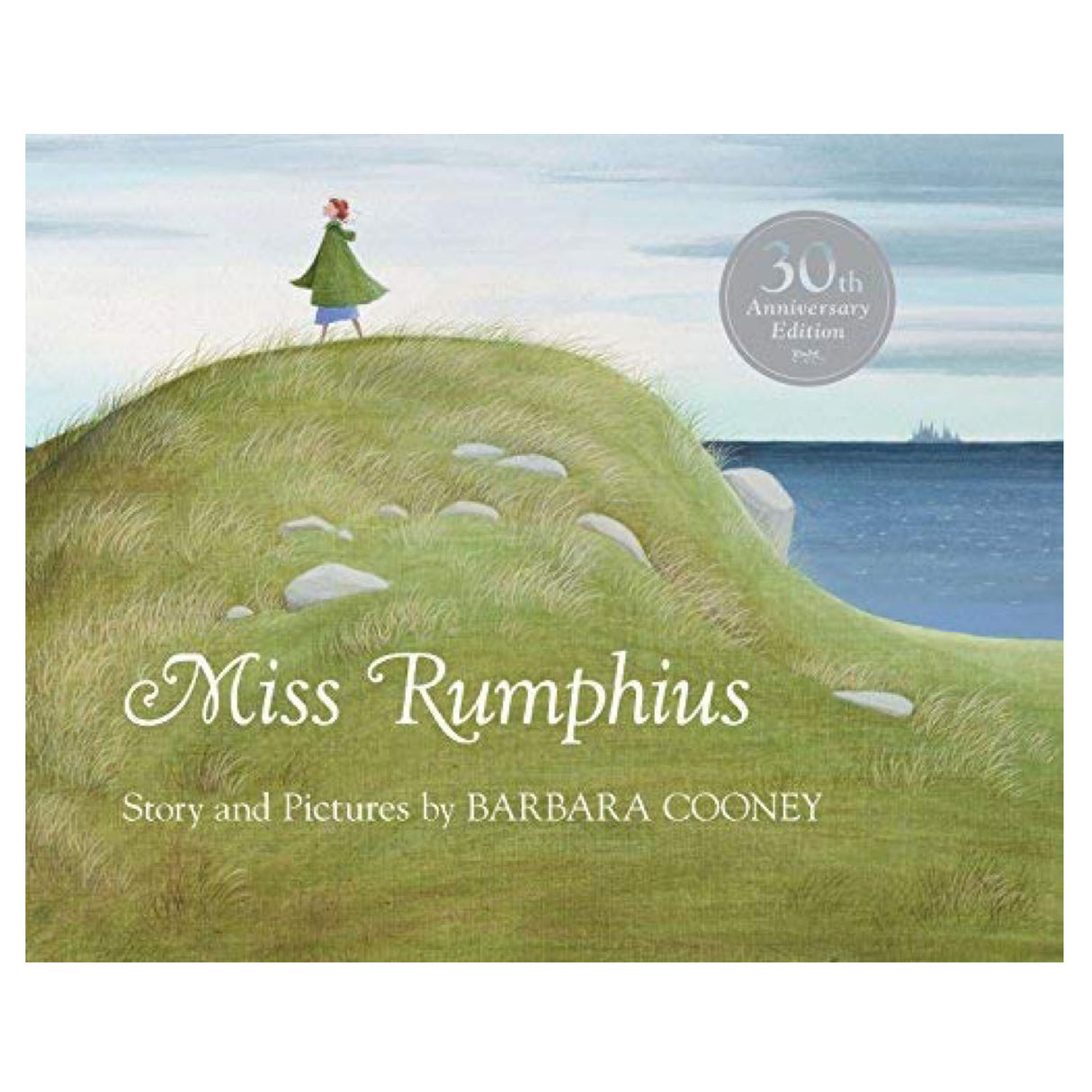 Miss Rumphius book cover showing a woman standing on a grassy hill overlooking the sea under a cloudy sky.