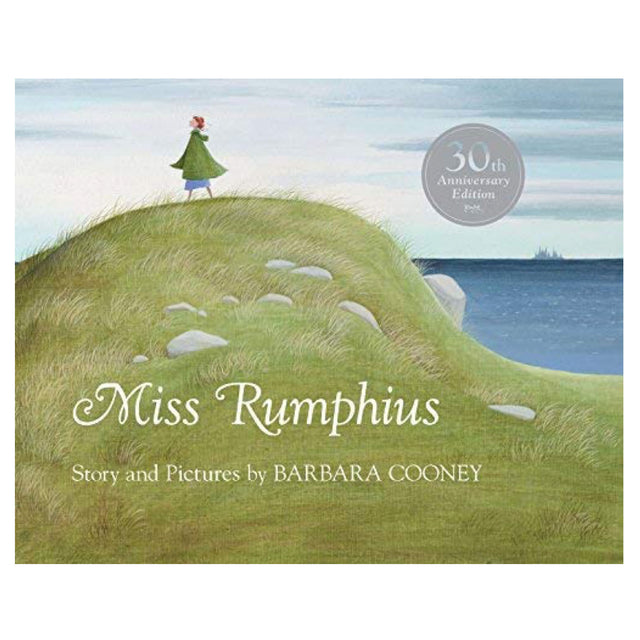 Miss Rumphius book cover showing a woman standing on a grassy hill overlooking the sea under a cloudy sky.